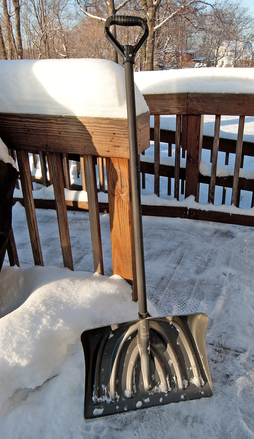 snow shovel resting on snowy backyard deck