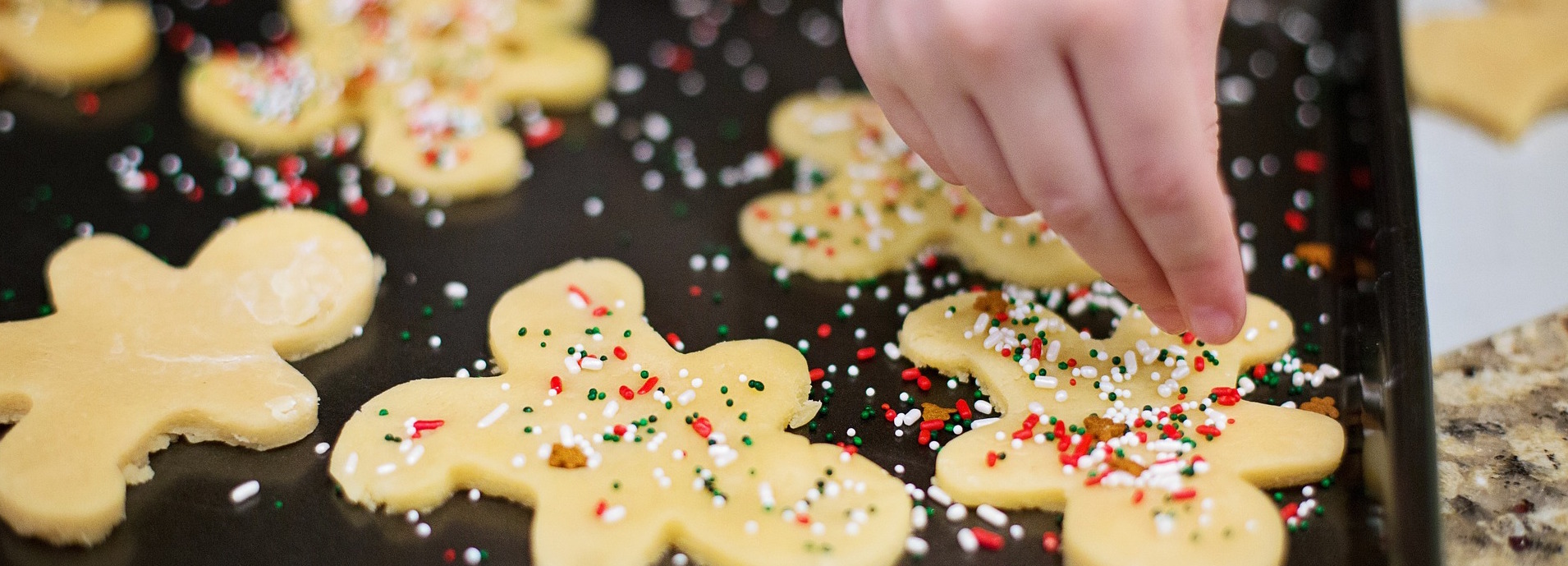 A photo of someone decorating a cookie with holiday sprinkles