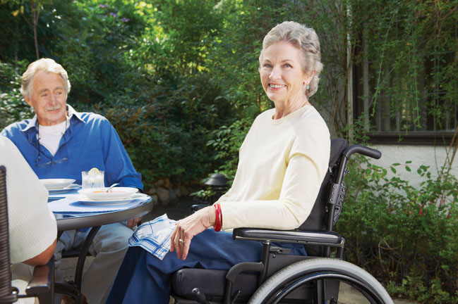 Older woman in wheelchair outdoors at table with others