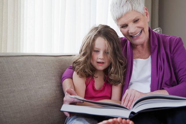 Older woman reading book to a young girl with arm around her